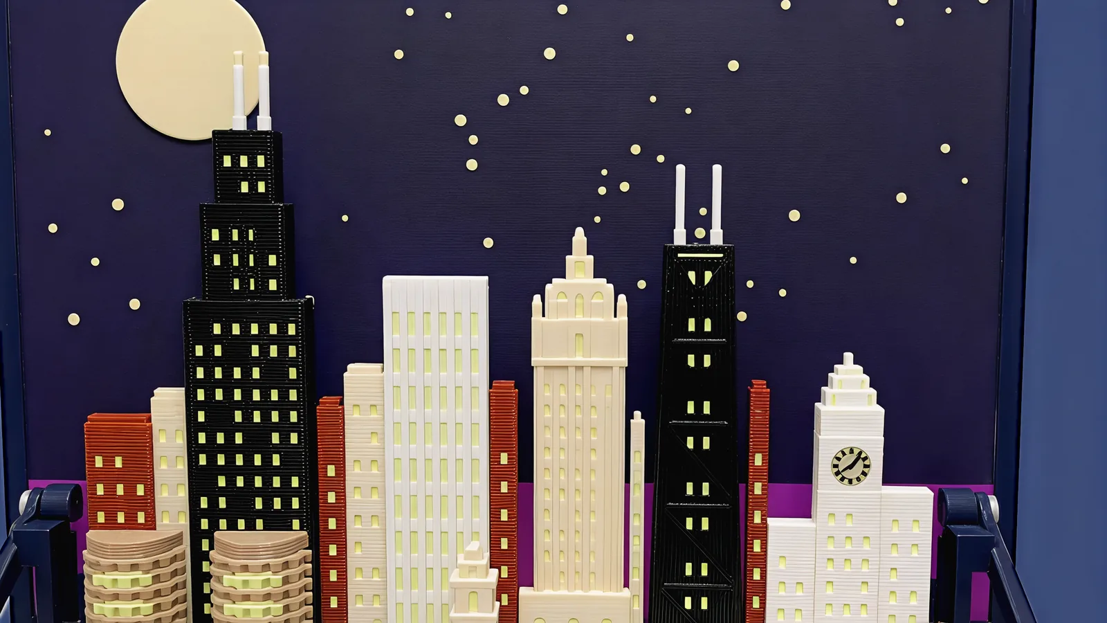 The skyline of the Chicago set under a large pale moon and cream stars on a dark indigo panel: at the left a black stepped tower with lit windows and two white antennas, the tallest; a plain white ribbed slab with lit window strips; a cream tower with a stepped Gothic crown and arched windows; a black tapering tower with faint X-braces, a lit band under its roof and two white antennas; at the right a white clock tower with a pale clock face marked with ticks and two hands, between lower white wings; slim brick-red and cream towers between them; at the bottom left the tops of two round tan towers ringed with balconies