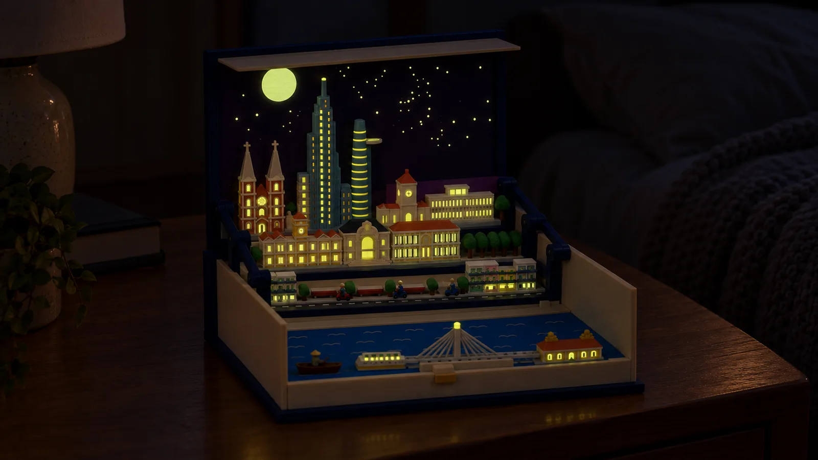 The open book with the Ho Chi Minh City pack on a bedside table in a dark bedroom, its moon, stars and windows glowing