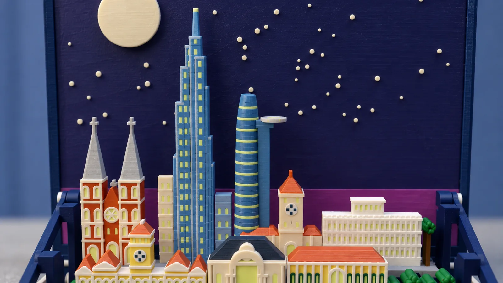 The skyline of the Ho Chi Minh City set under a large pale moon and cream stars on a dark indigo panel: at the left two red-brick towers banded in cream under gray spires with crosses, a round rose window between them; a cream filler tower; a very tall stepped tower of blue shafts with pale yellow-green windows rising to a slim crown; a tapering blue tower wrapped in pale bands with a round pale helipad on its right; a cream clock tower under a terracotta roof; a long white building with rows of windows and a small pavilion on top; in front, the top of a yellow hall with a clock tower and terracotta roofs, a cream theater under a dark slate roof and a yellow building with a terracotta roof