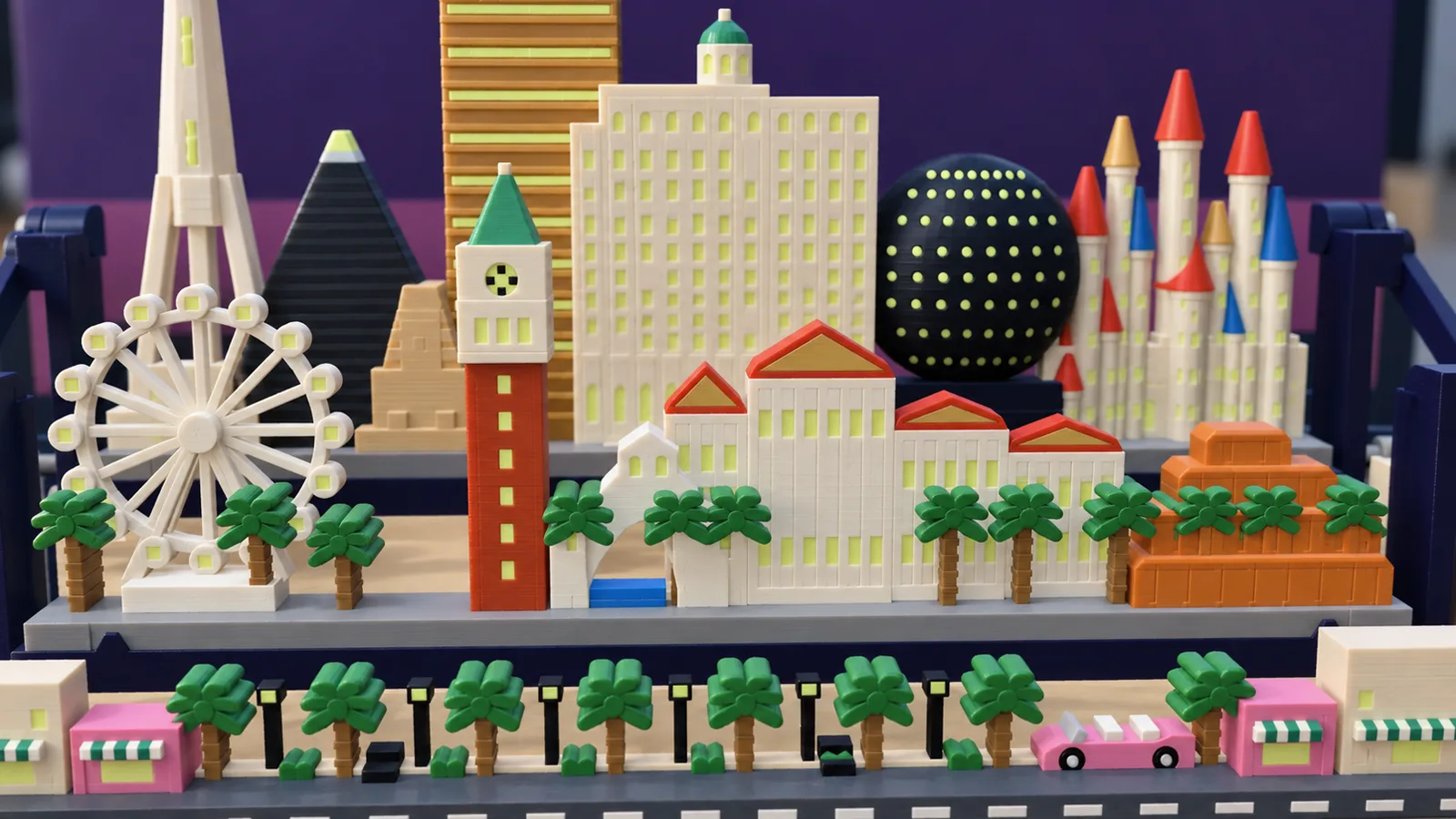 The middle row of the Las Vegas set: at the left a white spoked wheel with round cabins on two slanted legs; a brick-red bell tower with a cream belfry and a green spire; a white arched bridge over a strip of blue water; cream blocks lined with columns under red roofs with gold pediments; a terracotta stepped mesa at the right; green palms all along the row; behind, the tall cream tower, the dark pyramid and sphinx, the bronze tower, the cream stepped building, the dotted globe and the castle towers; below, the boulevard with cream and pink shops under teal-and-white striped awnings, black lamps, hedges, palms and a pink convertible