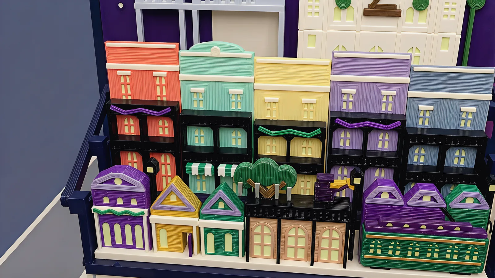 Close-up of the galleries: coral, mint, butter, lilac and sky-blue townhouses with black iron balconies and purple and green bead swags, the striped awning, small purple, gold and green gabled houses, the live oak and the green streetcar in front