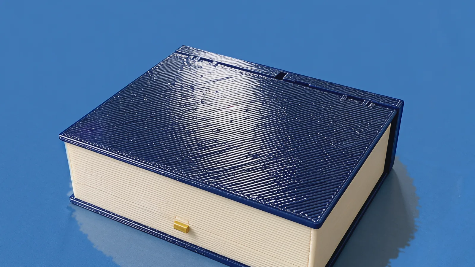 The closed Moonlit Atlas book: navy cover, cream page block and a brass button