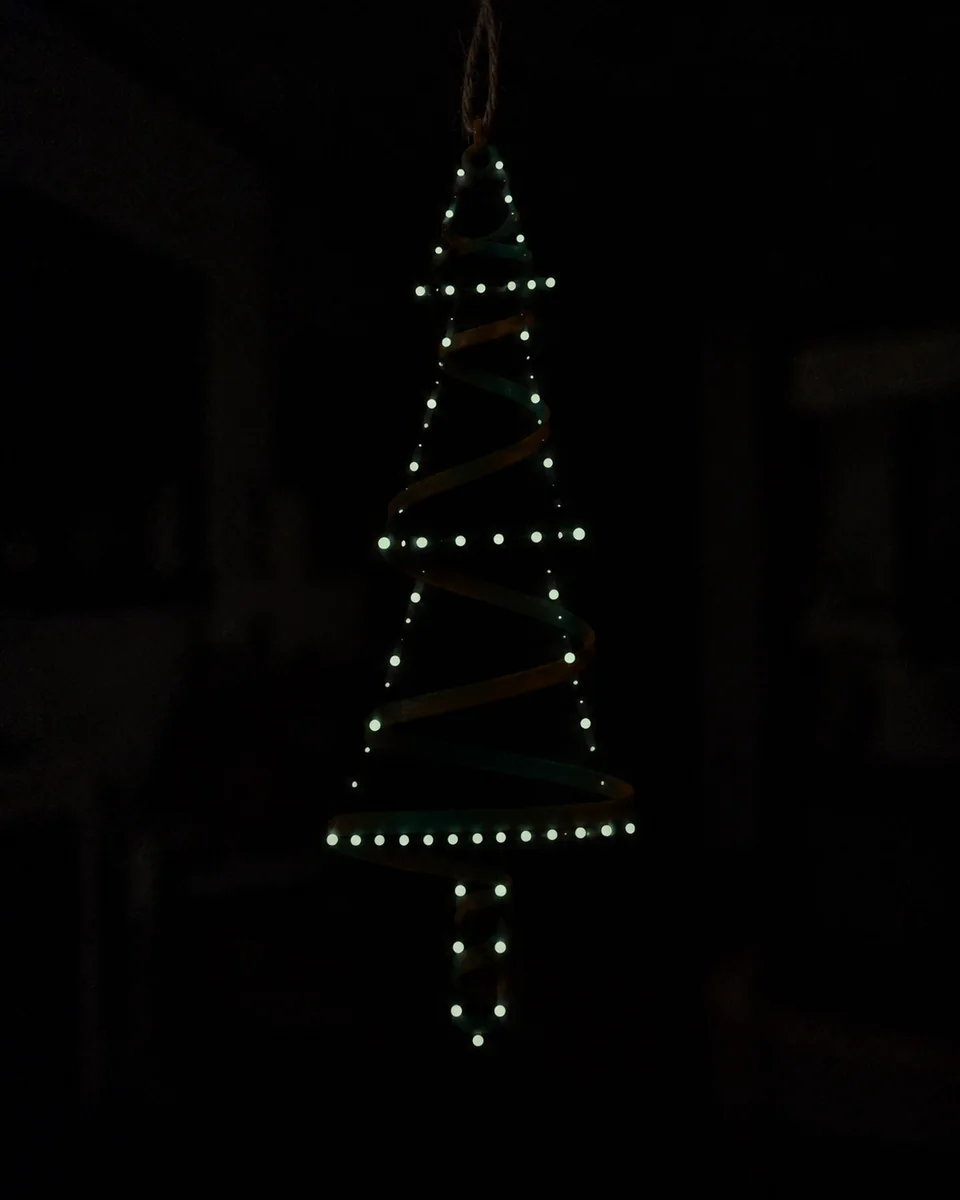 In a dark room, glowing dots trace a tiered pine tree, with the body faintly visible behind them